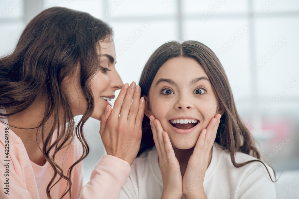 Mom whispers in ear of enthusiastic surprised daughter Mom whispers in ear of enthusiastic surprised daughter