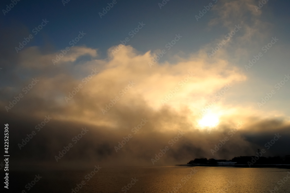Golden morning mist over the calm water of the lake. Fascinating clouds and fog over the water. Murmansk, Russia