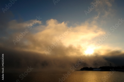 Golden morning mist over the calm water of the lake. Fascinating clouds and fog over the water. Murmansk, Russia