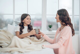 Mom giving drink to daughter sitting in bed