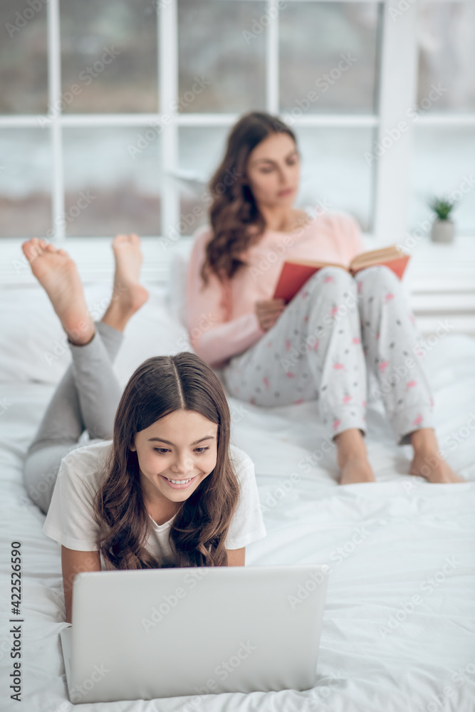 Girl at laptop and mom reading book Girl at laptop and mom reading book