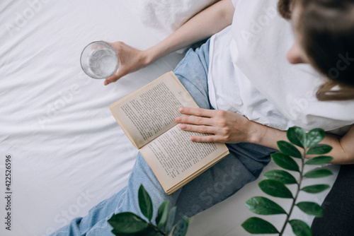 A young woman in casual clothes spends time reading a book and holding a glass of water top view