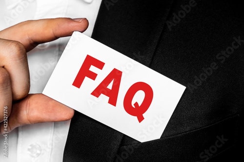 A man in a black business suit lowers or removes from his breast pocket a white business card with the inscription FAQ frequently asked questions. Business concept