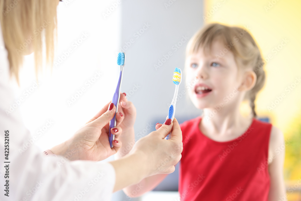 Doctor holding two toothbrushes in front of little girl