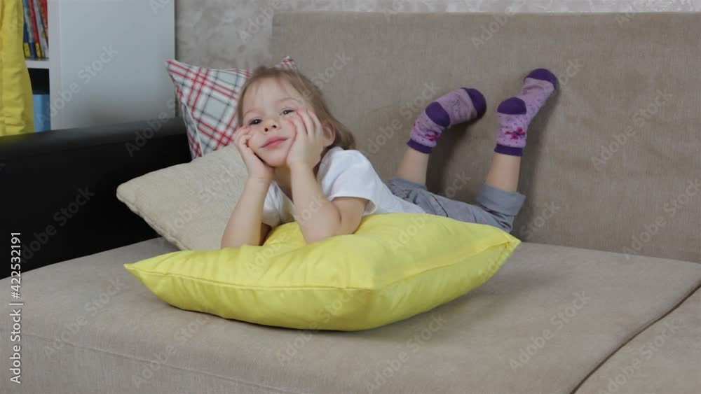 a large portrait of a little girl lying on a sofa leaning on a yellow pillow moving her legs a large portrait of a little girl lying on a sofa leaning on a yellow pillow moving her legs