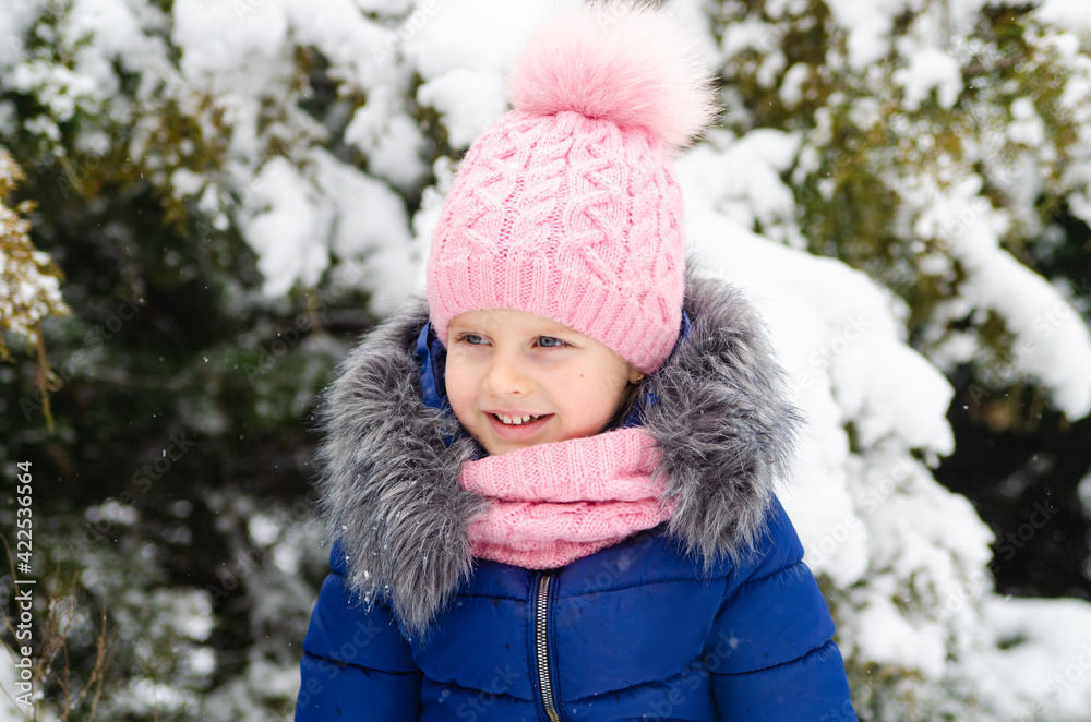 A girl in a pink hat plays with snow. Holidays with a child in winter