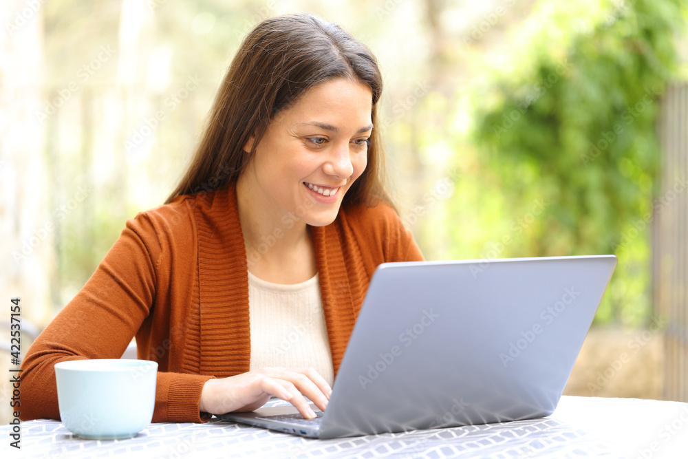 Happy woman browsing laptop in a house terrace Happy woman browsing laptop in a house terrace