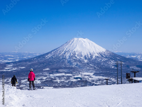 Skiers looking at snowy volcano and town on a clear day in early spring (Niseko Hanazono Resort, Hokkaido, Japan) photo
