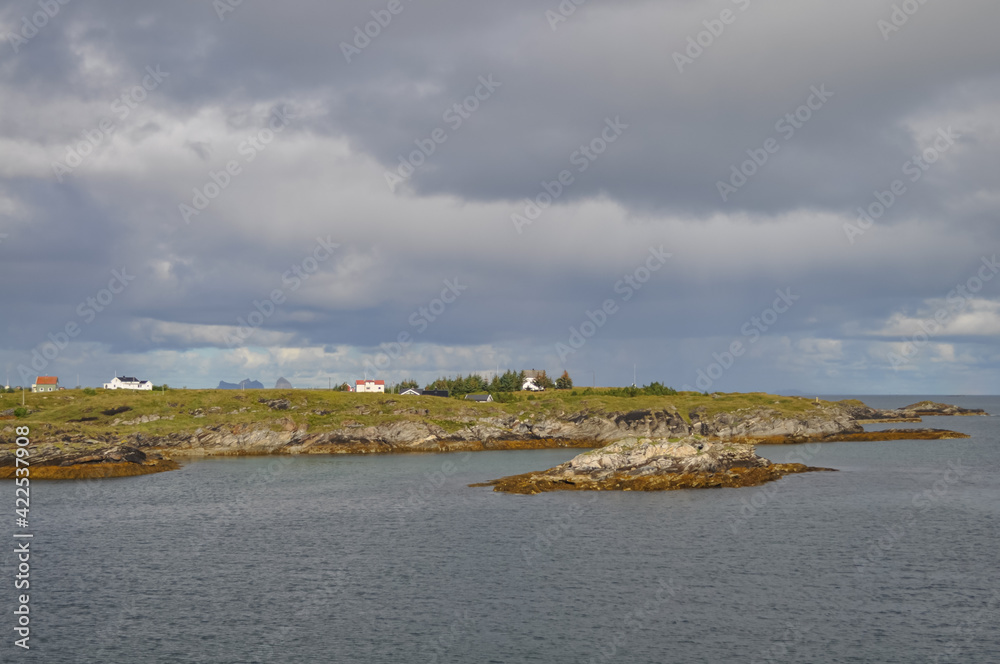 
View from ferry to the small fishermen village on island in Helgeland archipelago in the Norwegian sea on sunny summer morning. Silhouette of Træna island on the background