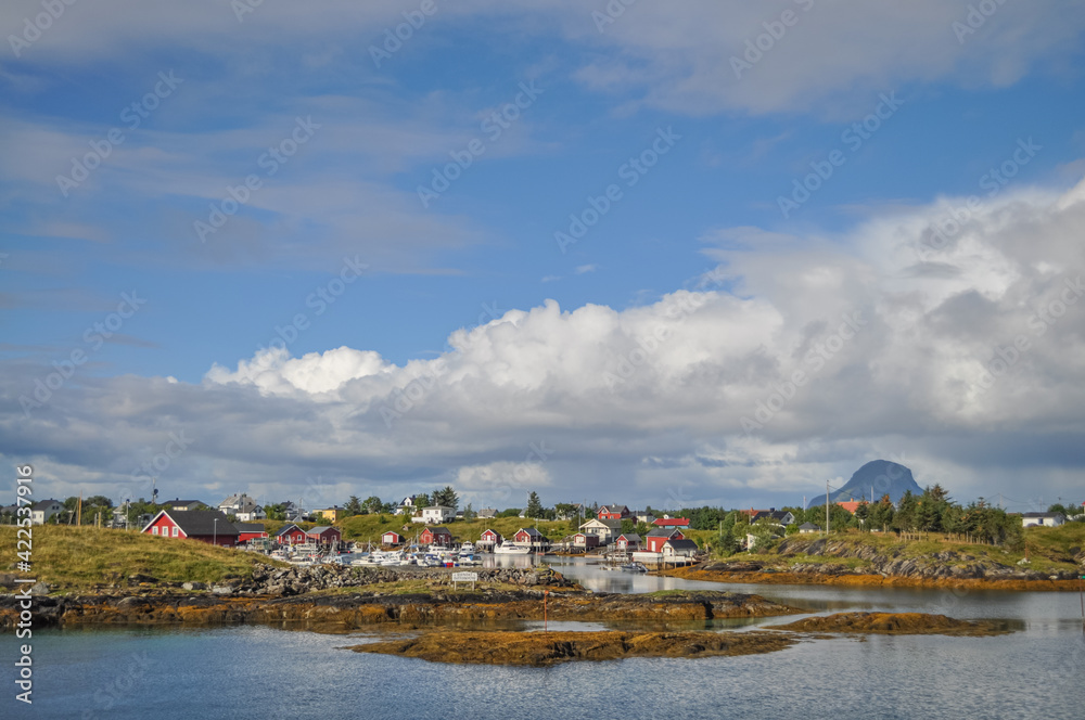 View from ferry to the small fishermen village on island in Helgeland archipelago in the Norwegian sea on sunny summer morning. Silhouette of Lovund island on the background
