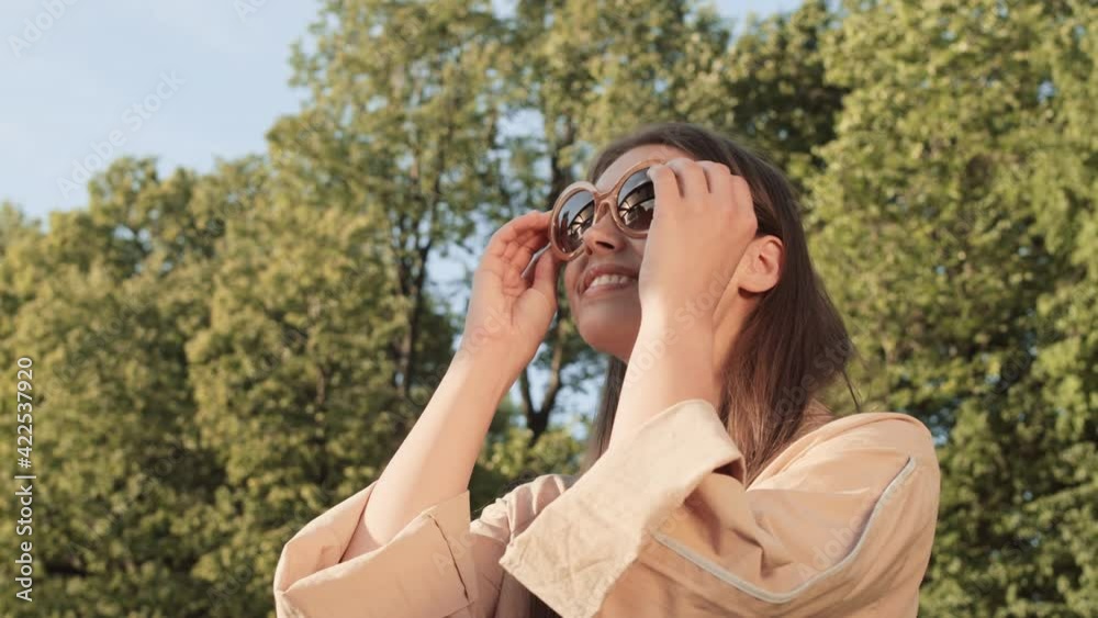 Chest-up POV of young happy Caucasian female person smiling, sitting in sunny summer park, taking sunglasses off, then snapping fingers, pointing finger, winking and looking on camera Chest-up POV of young happy Caucasian female person smiling, sitting in sunny summer park, taking sunglasses off, then snapping fingers, pointing finger, winking and looking on camera