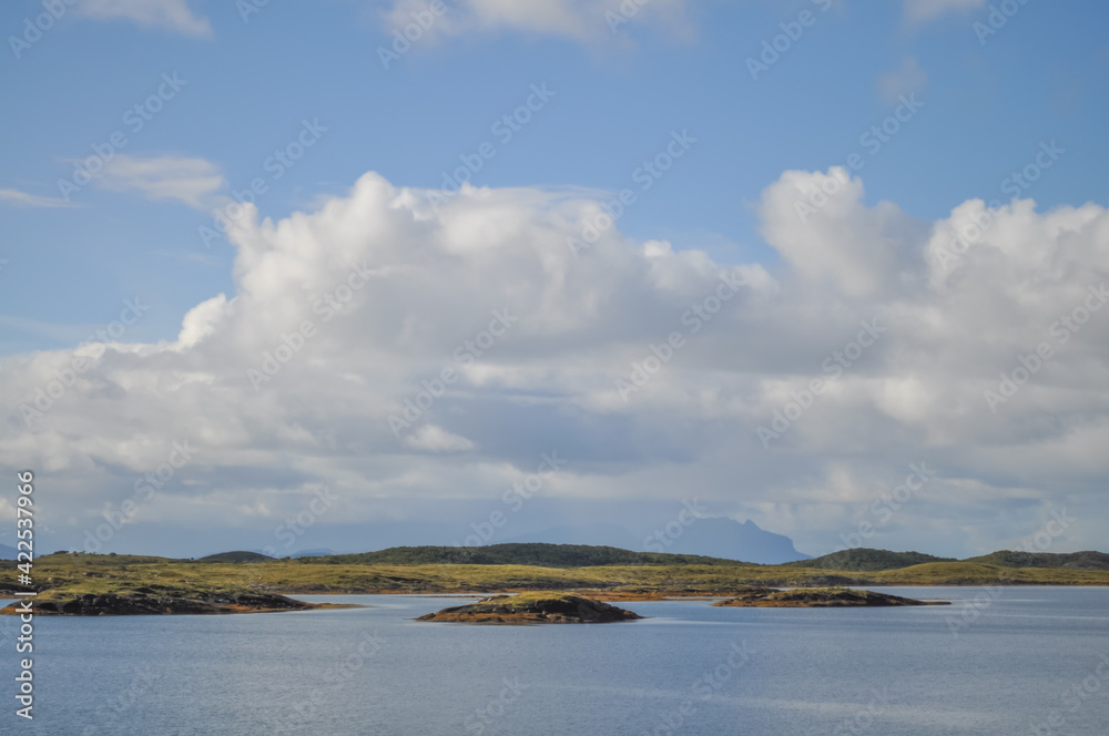 
View from ferry to the small rocky islands of Helgeland archipelago in the Norwegian sea on sunny summer morning. White clouds over the blue sea