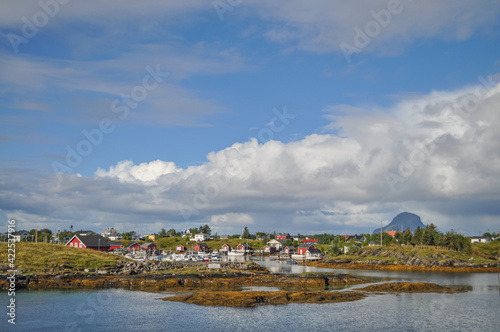 View from ferry to the small fishermen village on island in Helgeland archipelago in the Norwegian sea on sunny summer morning. Silhouette of Lovund island on the background 