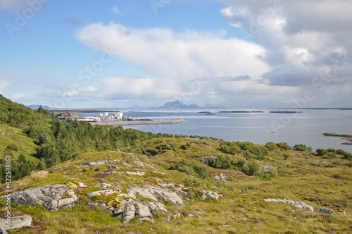 View from Lovund hills to the rocky coastline of Lovundf and Lovund harbor on sunny summer morning. White clouds over the blue sea. Donna island on the horizon. © Ilga