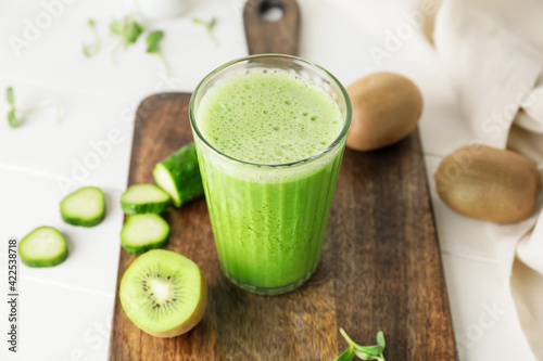 Glass of tasty green smoothie and ingredients on light background, closeup