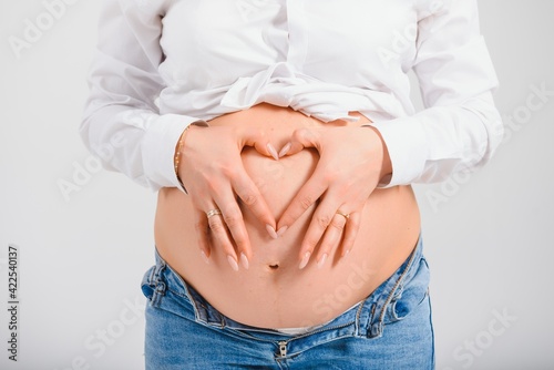 Pregnant Woman holding her hands in a heart shape on her baby bump. Pregnant Belly with fingers Heart symbol. Maternity concept. Baby Shower