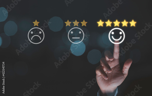 Businessman touching smile face icons with five gold stars on blue bokeh background, customer satisfaction for product and service concept.