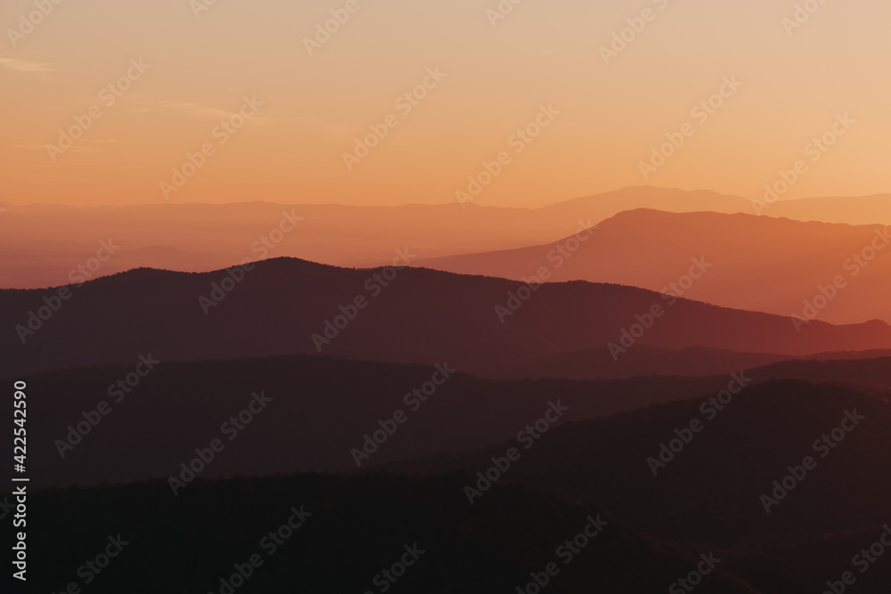 A vibrant citrus orange, yellow, deep purple sunset over the layers of the Appalachian Mountain range from Shenandoah National Park, Virginia, USA. A vibrant citrus orange, yellow, deep purple sunset over the layers of the Appalachian Mountain range from Shenandoah National Park, Virginia, USA.