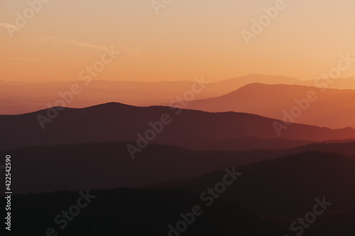 A vibrant citrus orange, yellow, deep purple sunset over the layers of the Appalachian Mountain range from Shenandoah National Park, Virginia, USA.