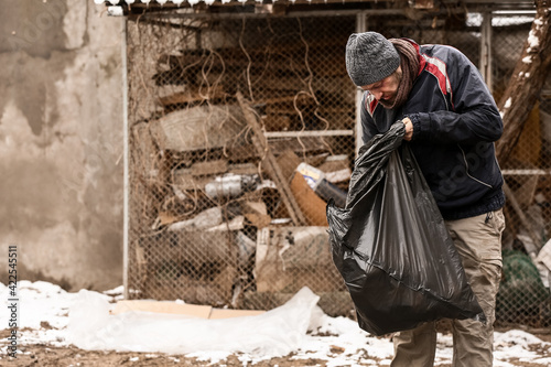 Poor homeless man with trash bag outdoors on winter day