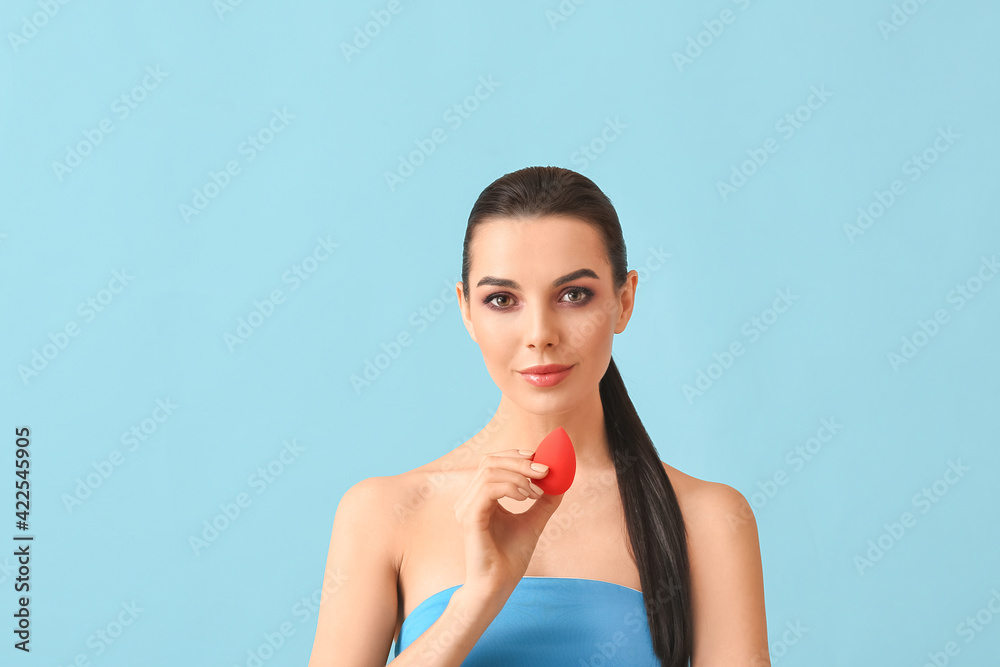 Beautiful young woman with makeup sponge on color background Beautiful young woman with makeup sponge on color background