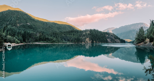 Panorama of the sun rising over the calm turquoise blue waters of Diablo Lake in North Cascades National Park, Washington, USA.