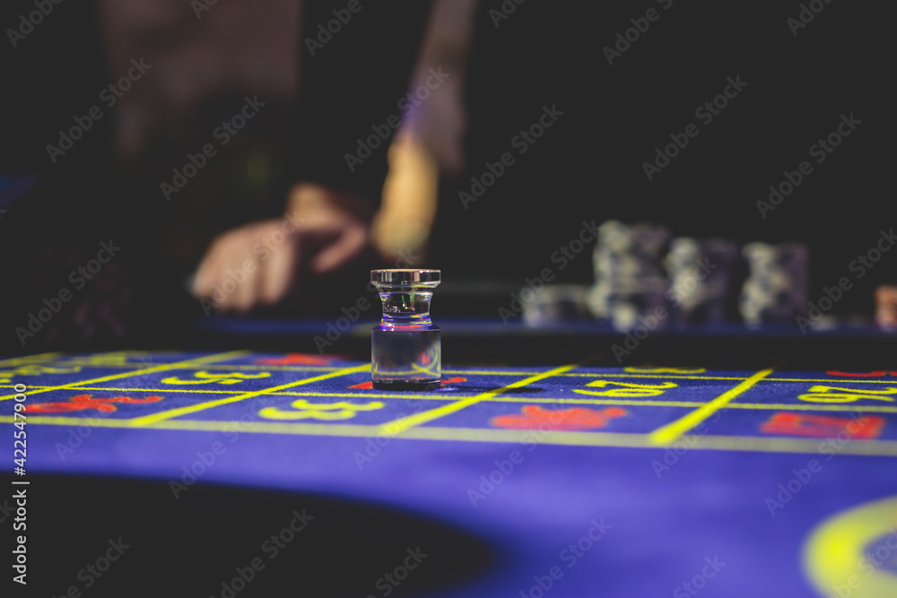 Naklejka premium A close-up vibrant image of multicolored casino table with roulette in motion, with casino chips. the hand of croupier, money and a group of gambling rich wealthy people playing in the background