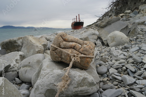 An old bobber from styrofoam with barnacles attached amongst pebbles and blurred old ship in the background