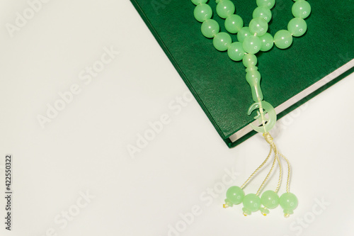 Islamic rosary beads of green color lie on the holy book of Muslims on a white background