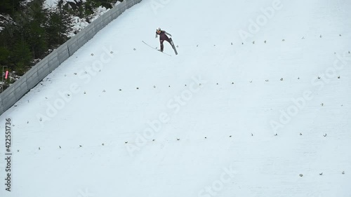 Winter ski jump ramp in Kranj, Slovenia. Jumper runs down to generate sufficient speed before reaching the jump. Person glide down on tracks along the in-run. Static shot, slow motion