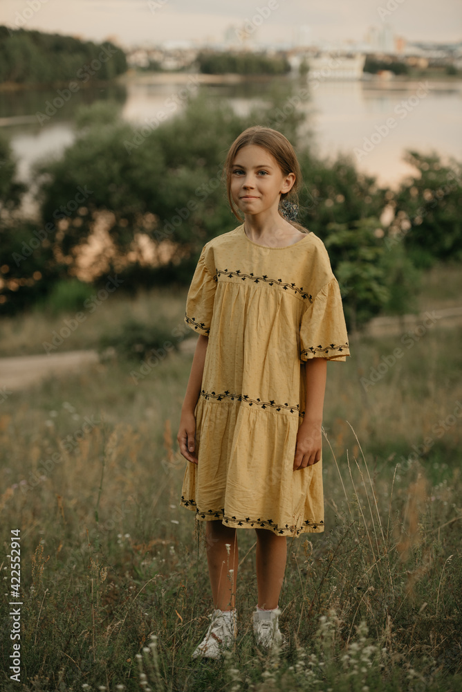 A close portrait of a happy girl in a dress in full length on the hillside against the lake at sunset. A close portrait of a happy girl in a dress in full length on the hillside against the lake at sunset.