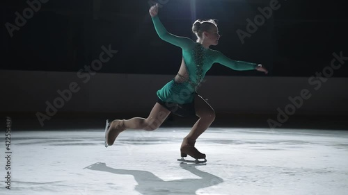 junior female figure skater is performing alone on ice rink, young sporty girl is doing jumps and flips, slow motion shot photo