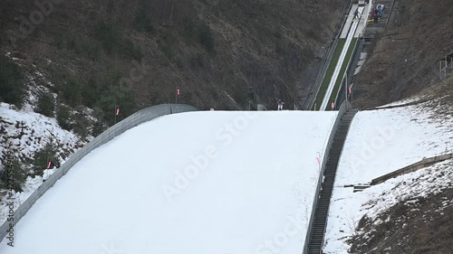 Winter ski jump ramp in Kranj, Slovenia. Jumper runs down to generate sufficient speed before reaching the jump. Person glide in the air over landing slope. Static shot, slow motion