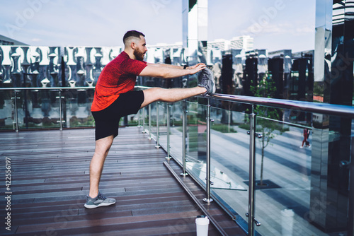 Sportsman stretching legs on balcony over city