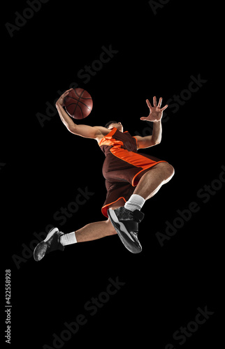 Print op canvas Young professional basketball player in action, motion isolated on black background, look from the bottom