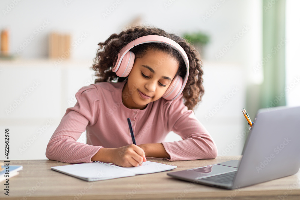 African american schoolgirl having online lesson, using laptop and headphones at home, taking notes African american schoolgirl having online lesson, using laptop and headphones at home, taking notes