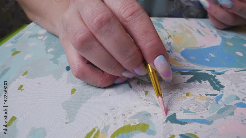 The girl paints a picture by numbers with paints with a brush, in motion, close-up. The girl paints a picture by numbers with paints with a brush, in motion, close-up.