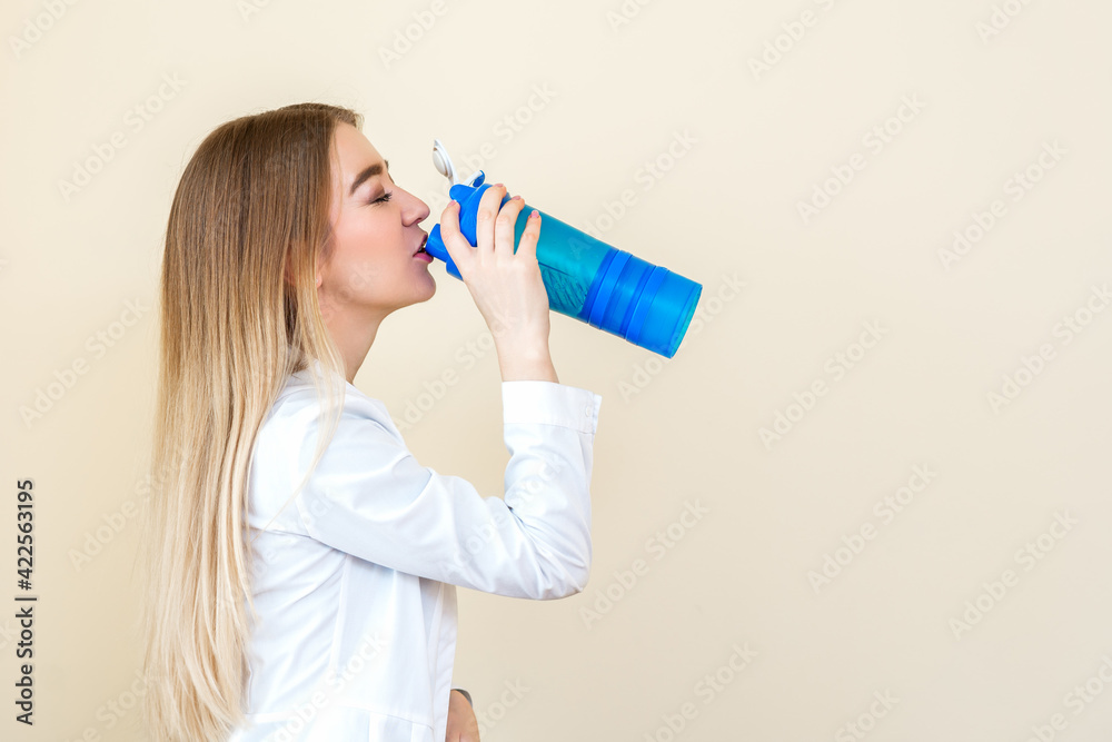 Side view of beautiful young caucasian woman is drinking water from plastic bottle against a beige background Side view of beautiful young caucasian woman is drinking water from plastic bottle against a beige background
