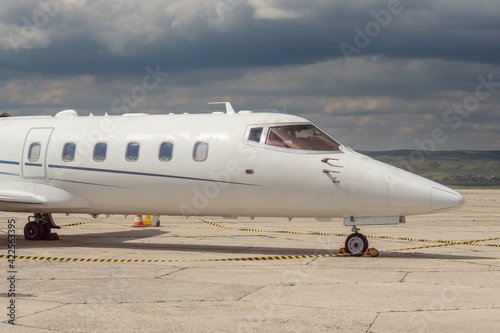 Side view of front part of white business airplane with jet engines. Attractive cloudy sky over the airport. Modern technology in fast transportation, business travel and tourism, aviation.