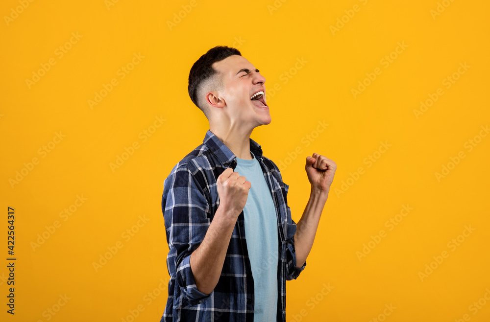 Overjoyed millennial guy making YES gesture with both hands, feeling triumphant over achievement on orange background Overjoyed millennial guy making YES gesture with both hands, feeling triumphant over achievement on orange background