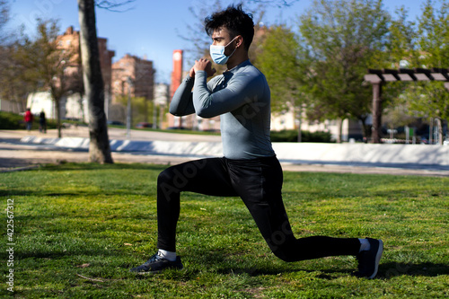 Young man with mask doing lunges in a park