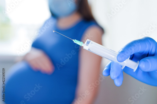 Pregnant Vaccination. Pregnant Woman In Face Mask Getting Vaccinated in Clinic. Doctor Giving Corona Virus Vaccine Injection Patient. Covid-19 Flu Protection. Selective focus. Syringe close up.