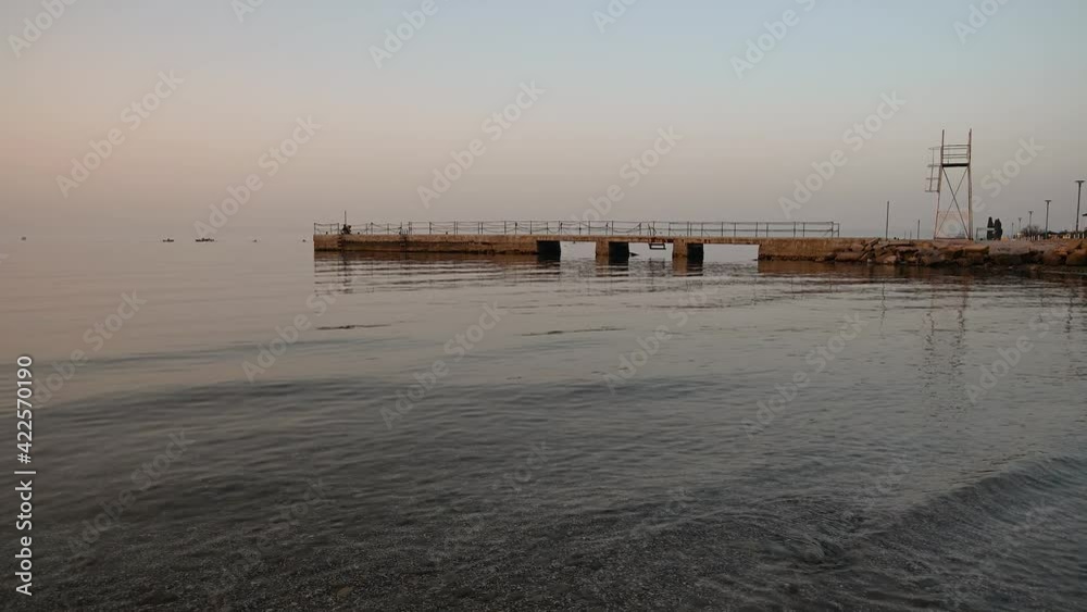San Simon bay, Slovenia: concrete pier with calm waves hitting pebble beach at sunset. Beautiful colors at golden hour. Static shot, real time, wide angle San Simon bay, Slovenia: concrete pier with calm waves hitting pebble beach at sunset. Beautiful colors at golden hour. Static shot, real time, wide angle