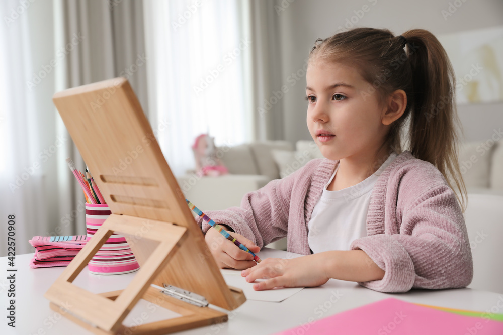 Adorable little girl doing homework with tablet at table indoors Adorable little girl doing homework with tablet at table indoors
