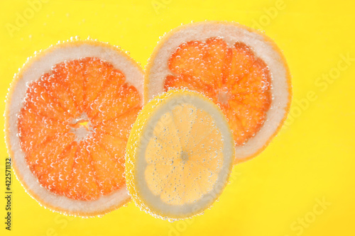 Slices of different citrus fruits in sparkling water on yellow background