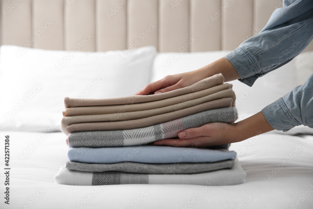 Woman with folded cashmere clothes on bed, closeup
