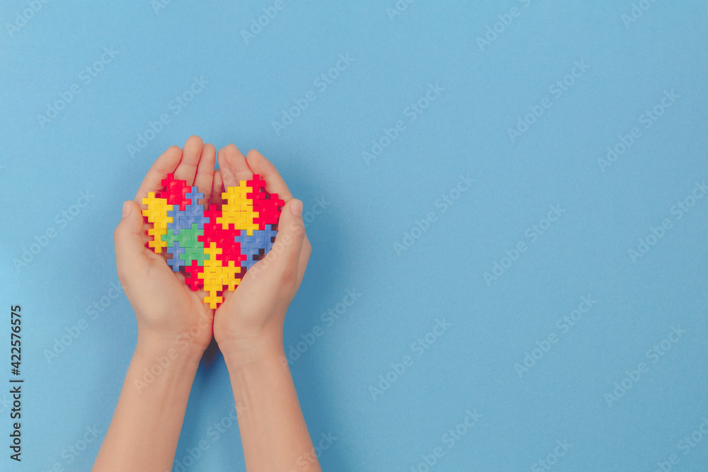 Kid hand holding colorful heart on light blue background. World autism awareness day concept Kid hand holding colorful heart on light blue background. World autism awareness day concept