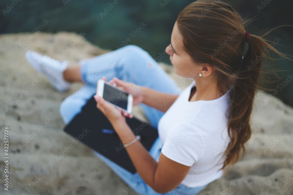 Top view of millennial hipster girl with modern smartphone technology pondering on text publication, teenage female blogger with mobile technology and sketchbook for learning resting outdoors Top view of millennial hipster girl with modern smartphone technology pondering on text publication, teenage female blogger with mobile technology and sketchbook for learning resting outdoors