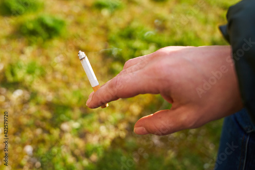 Mano sujetando un cigarrillo a medio uso sobre hierba verde © Your Pixels