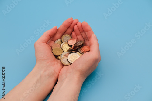 Hands full of coins on blue background. Closeup, copy space. Saving and earning money concept